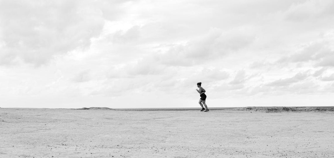 A lone runner on a vast, open terrain under a cloudy sky, captured in Natal, Brazil.
